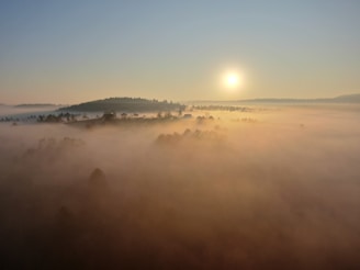 a foggy landscape with a sun in the background
