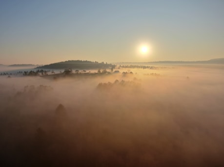 a foggy landscape with a sun in the background