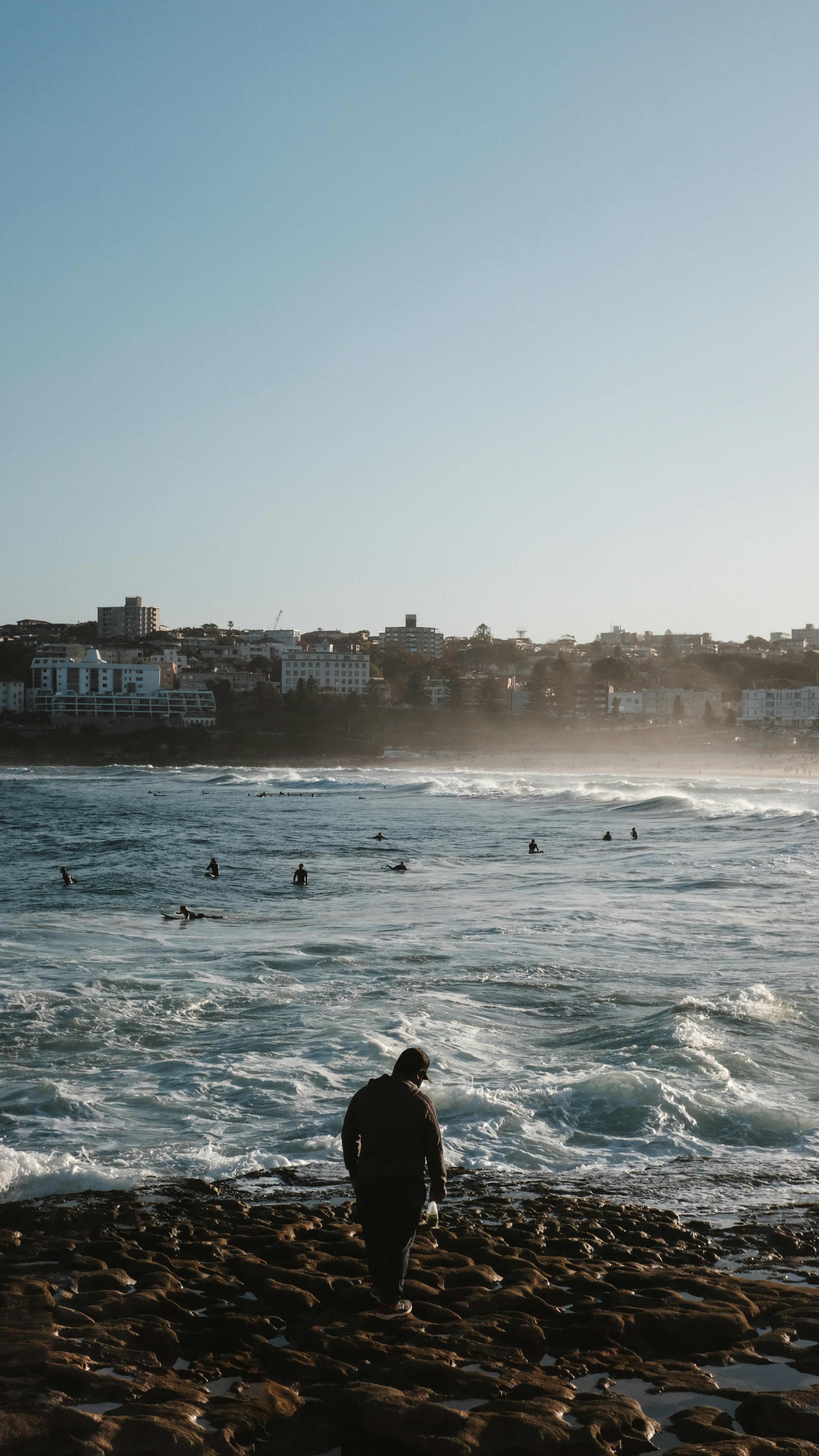 Eine Person, die an einem felsigen Strand steht und auf ein Gewässer schaut