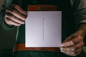 Close-up of elegant hands holding a card with golden typography on a dark textured background.