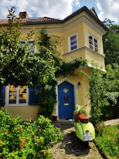 Yellow house exterior with a blue Vespa parked in front on a sunny day.
