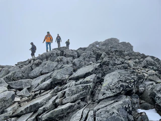 Hikers crossing a stream during a backcountry practice hike under cloudy skies.