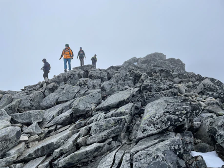 Hikers crossing a stream during a backcountry practice hike under cloudy skies.