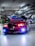 A customized red BMW car is parked in an indoor garage, featuring vibrant headlight modifications. The hood is adorned with graphics, and other cars with elaborate designs are visible in the background. The garage has numerous overhead lights and visible piping.
