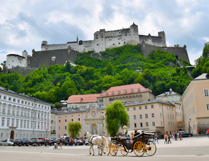 City square in Salzburg with horse and carriage in the foreground and Hihensalzburg Fortress behind