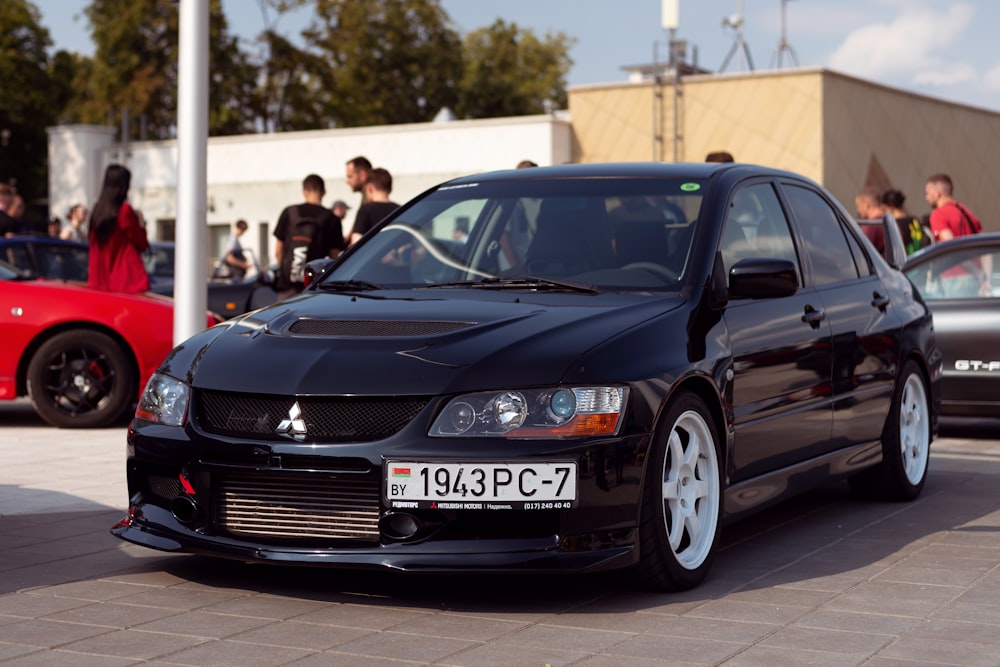 a black car parked in a parking lot with other cars and people