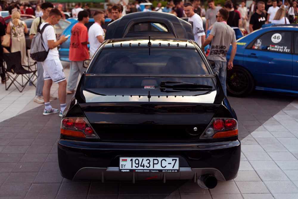 a black car parked in a parking lot with people standing around