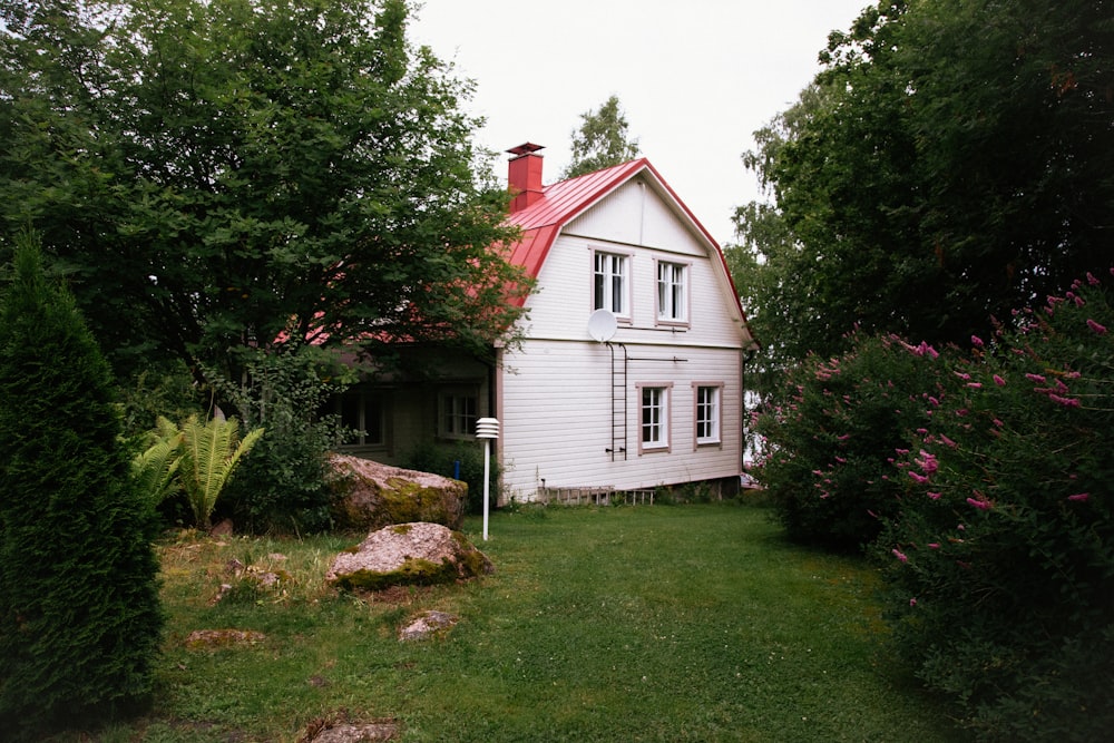 a white house with a red roof surrounded by trees and bushes