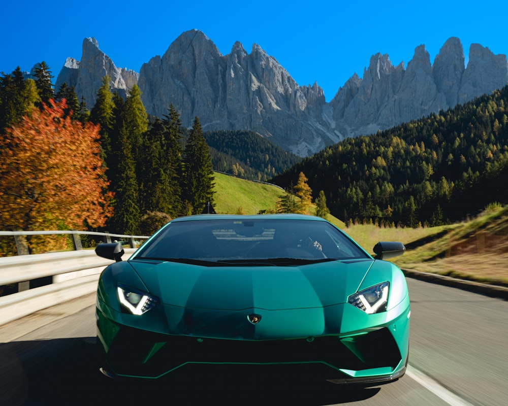 a green sports car on a road with trees and mountains in the background