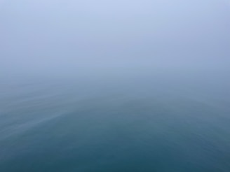 A minimalist seascape with muted tones reflecting a calm, foggy morning by the shore.