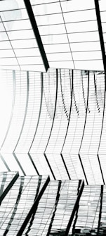 An abstract architectural structure with a pattern of curved glass panels and reflective surfaces creating a dynamic and modern aesthetic. The lines and shapes form an intricate, repeating pattern that plays with light and shadow.