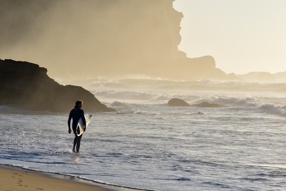 Un hombre cargando una tabla de surf en una playa