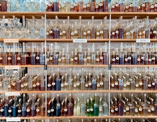 Shelves filled with a variety of bottles containing different types of spirits. Each shelf is labeled with categories such as 'Eau de Vie', 'Cognac', 'Whisky', and 'Rom'. The bottles are organized neatly by size and type, creating a visually appealing display.