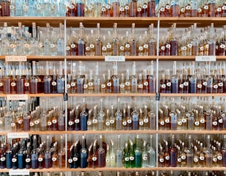 Shelves filled with a variety of bottles containing different types of spirits. Each shelf is labeled with categories such as 'Eau de Vie', 'Cognac', 'Whisky', and 'Rom'. The bottles are organized neatly by size and type, creating a visually appealing display.