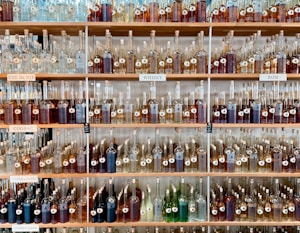 Shelves filled with a variety of bottles containing different types of spirits. Each shelf is labeled with categories such as 'Eau de Vie', 'Cognac', 'Whisky', and 'Rom'. The bottles are organized neatly by size and type, creating a visually appealing display.