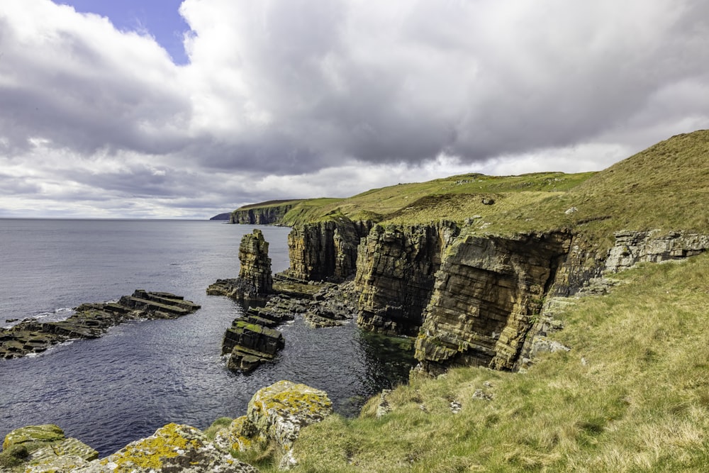 a cliff side with a body of water and a grassy hill