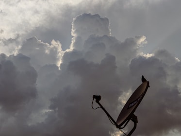 Dark, dramatic clouds cover the sky with a satellite dish in the foreground. The clouds are dense and appear to be lit from behind, creating a halo effect.