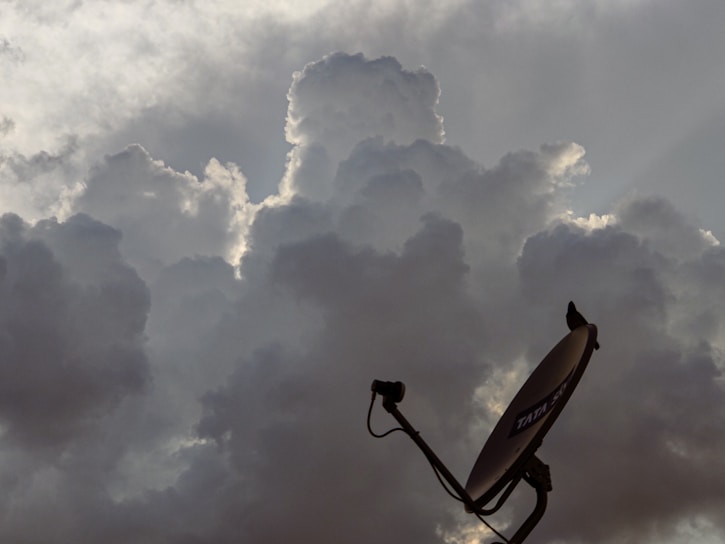 Dark, dramatic clouds cover the sky with a satellite dish in the foreground. The clouds are dense and appear to be lit from behind, creating a halo effect.