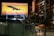 A nighttime urban scene featuring a large illuminated billboard showcasing an airplane with the text 'WORLD'S FASTEST AIRPLANES. BUILT IN ATL.' The background of the billboard depicts a city skyline at sunset. Nearby is a building with a vertical neon sign labeled 'PONCE.' The street below is moderately lit, with a car on the road and a sign reading 'EATS' on a wall.