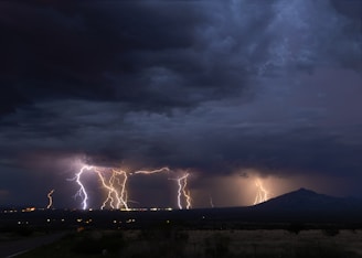 Multiple lightning forks branching across a deep blue sky above a mountain range.