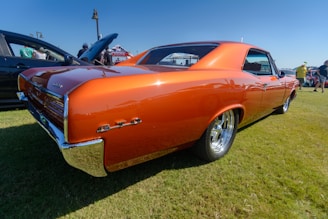 A shiny red 1967 Pontiac GTO parked under a sunny blue sky at a classic car show.
