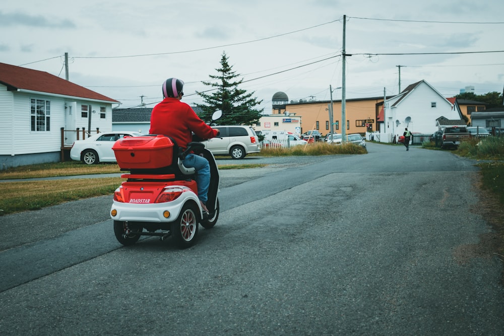 a person riding a red and white scooter on a street
