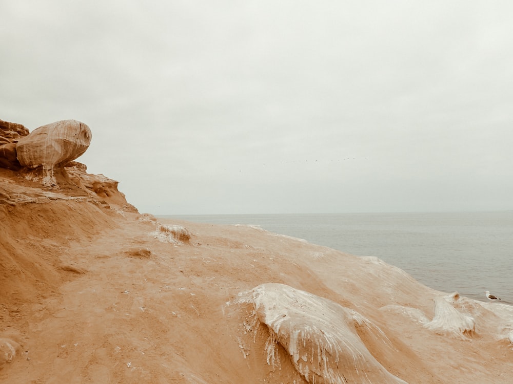 a sandy beach with a large rock on the shore