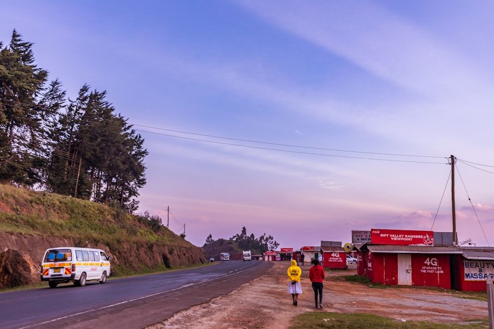 a group of people walking down a dirt road next to a building