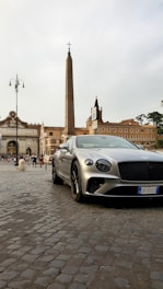 A sleek black luxury car parked in front of Rome's iconic Colosseum at dusk.