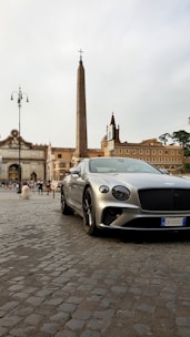 A sleek black luxury car parked in front of Rome's iconic Colosseum at dusk.