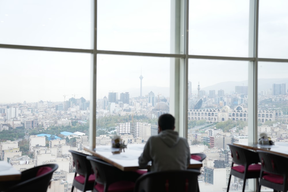 a person sitting at a table looking out a window at a city