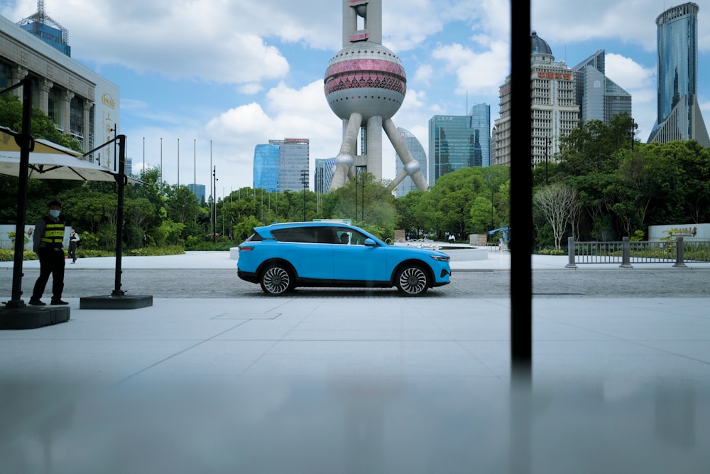 Une voiture bleue garée dans un parking avec une ligne d’horizon de la ville en arrière-plan
