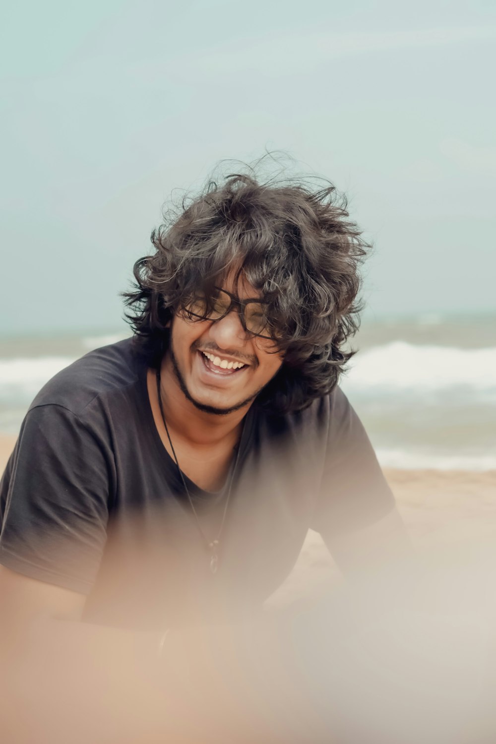 a man with curly hair and sunglasses on a beach