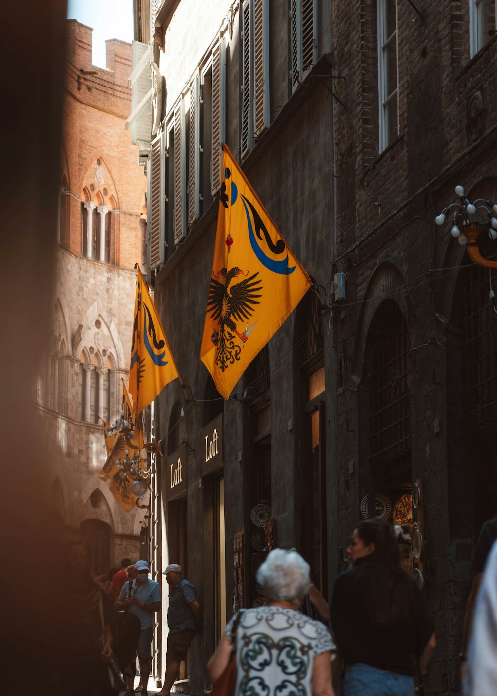 a group of people walking down a narrow street with a flag on a pole