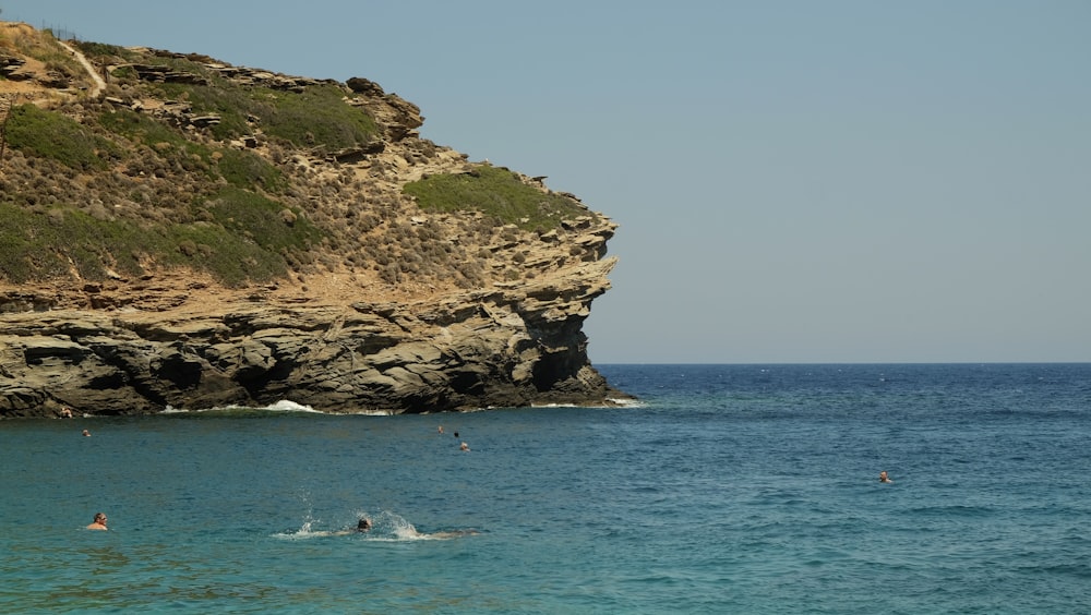 a group of people swimming in the ocean by a rocky cliff