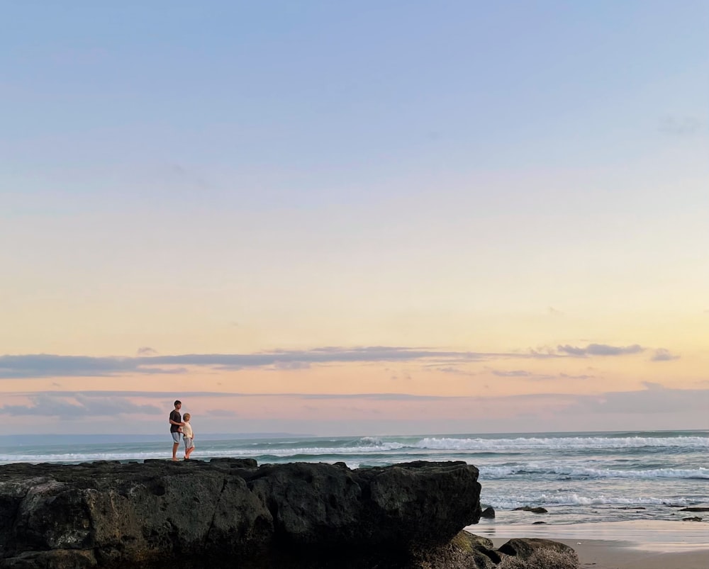 a couple people standing on a rock by the water