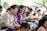 A group of people sitting closely together, each holding and reading from books. They appear to be focused and engaged, dressed in colorful, traditional clothing. The scene suggests a cultural or community gathering, possibly a workshop or seminar.