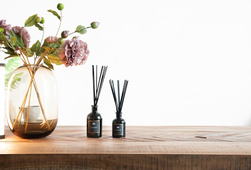 a vase with flowers and scented diffusers on a wooden table