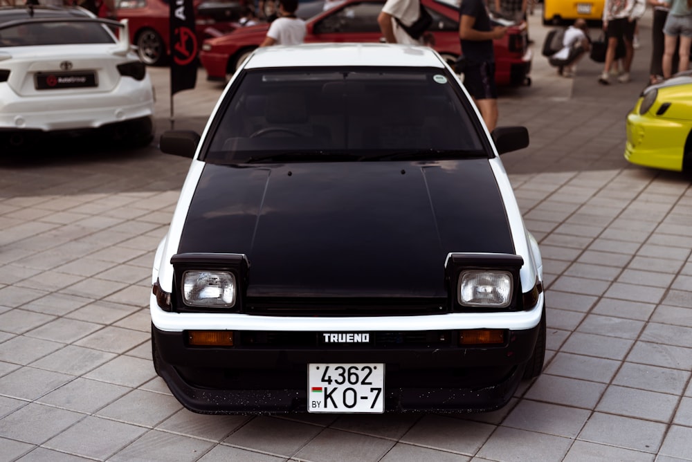 a black car parked on a brick surface with other cars in the background