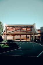 A modern building with a unique architectural design featuring a large, open entrance and curved elements on the sides. The structure is surrounded by carefully manicured greenery and a smooth asphalt driveway with clearly marked lanes and signage.