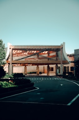 A modern building with a unique architectural design featuring a large, open entrance and curved elements on the sides. The structure is surrounded by carefully manicured greenery and a smooth asphalt driveway with clearly marked lanes and signage.