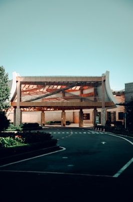 A modern building with a unique architectural design featuring a large, open entrance and curved elements on the sides. The structure is surrounded by carefully manicured greenery and a smooth asphalt driveway with clearly marked lanes and signage.