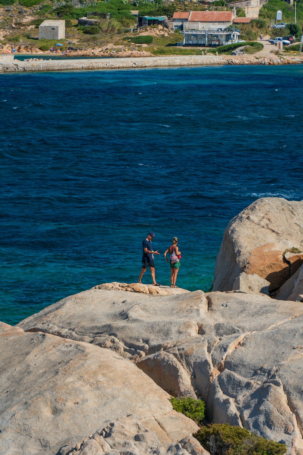 Un hombre y una mujer parados sobre rocas junto a un cuerpo de agua