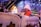 A group of children are enjoying a ride inside an amusement park decorated with winter-themed elements. One child wearing a white hat and orange jacket appears to be looking towards the camera with a smile. The background features festive lights, snowflakes, and structures designed to look like small houses with snowy roofs.