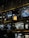 A multi-level shopping mall interior with various illuminated store signs, including those for a burger place and fashion brands. Decorative vertical hanging elements create an artistic effect. Warm ambient lighting complements the overall modern design.