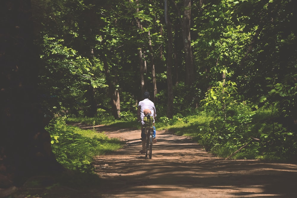 um homem andando de bicicleta em um caminho de terra na floresta