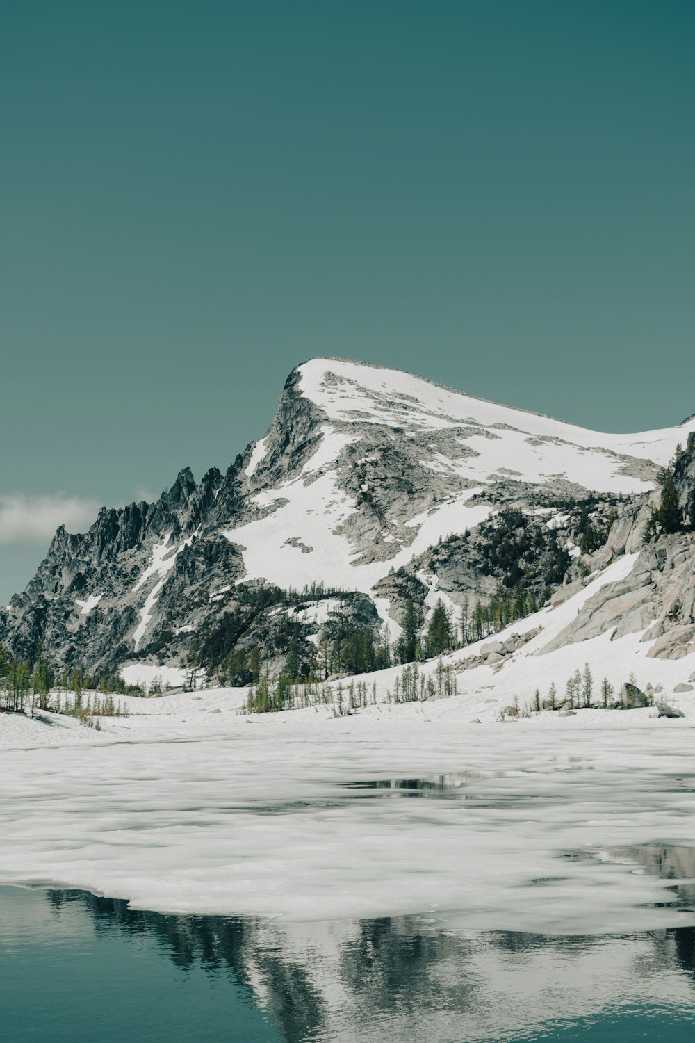 a snowy mountain with trees and water