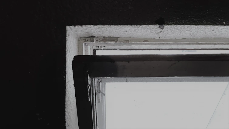 Close-up of a modern silver aluminium window frame reflecting natural light against a clean white wall.