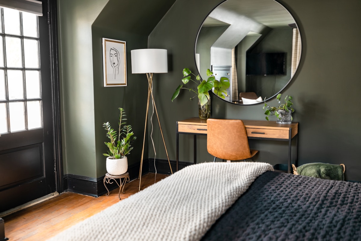 dark green accent wall bedroom with round mirror, floor lamp, and plants, no headboard