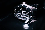 Close-up of a sleek black metallic watch reflecting soft white light.